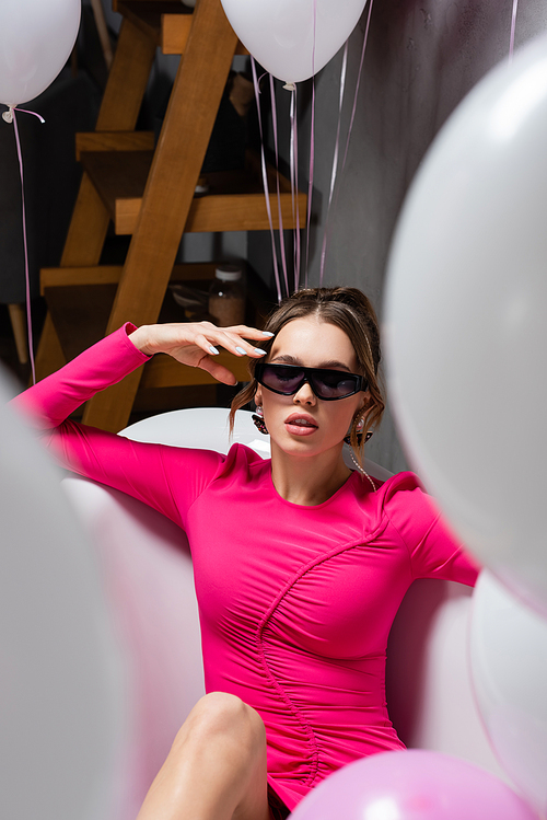 Stylish woman in sunglasses sitting in bathtub near balloons during party