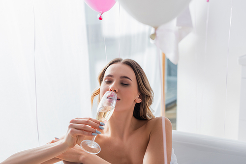 Woman drinking champagne while bathing near balloons at home