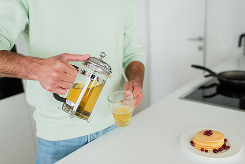 partial view of man pouring green tea near pancakes with cranberries in kitchen