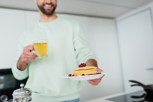 cropped view of happy blurred man holding green tea and plate with pancakes