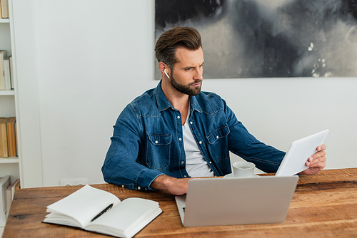 thoughtful freelancer holding digital tablet while working near laptop