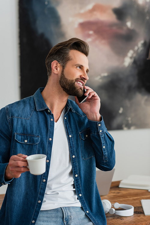 happy teleworker holding cup of coffee while talking on mobile phone
