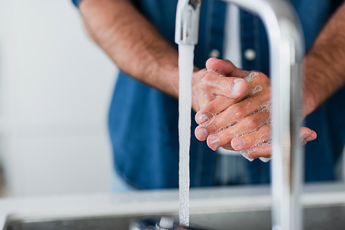 cropped view of blurred man washing hands with soap