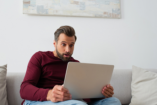 surprised man sitting on sofa and looking at laptop