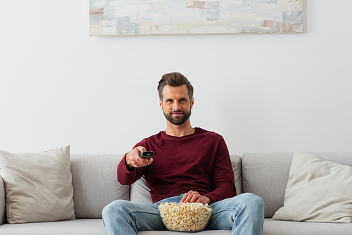 smiling man with bowl of popcorn watching tv on sofa at home