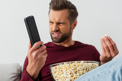 displeased man with popcorn looking at tv remote controller, blurred background