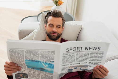 pleased man reading sport news on sofa at home