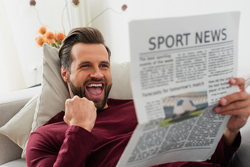 excited man showing triumph gesture while reading sport news at home