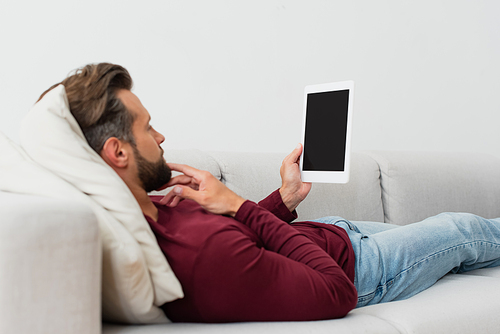 adult man holding digital tablet while resting on couch at home