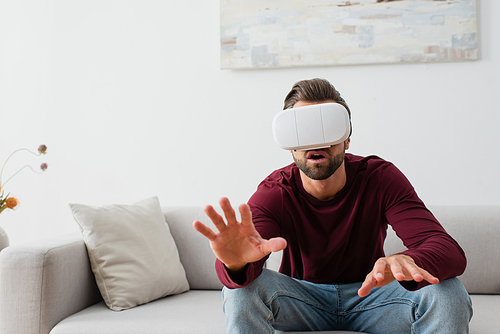 astonished man gesturing while sitting on couch in vr headset
