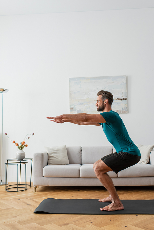 side view of man in sportswear practicing awkward pose on yoga mat