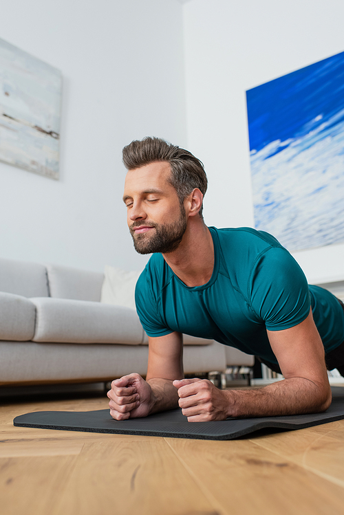 sportive man exercising in plank pose with closed eyes