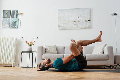 side view of man practicing pigeon pose on yoga mat at home