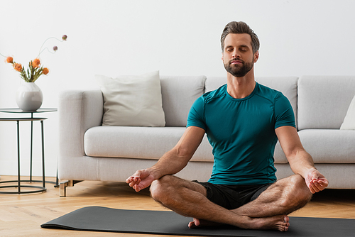 man with closed eyes meditating in lotus pose on yoga mat