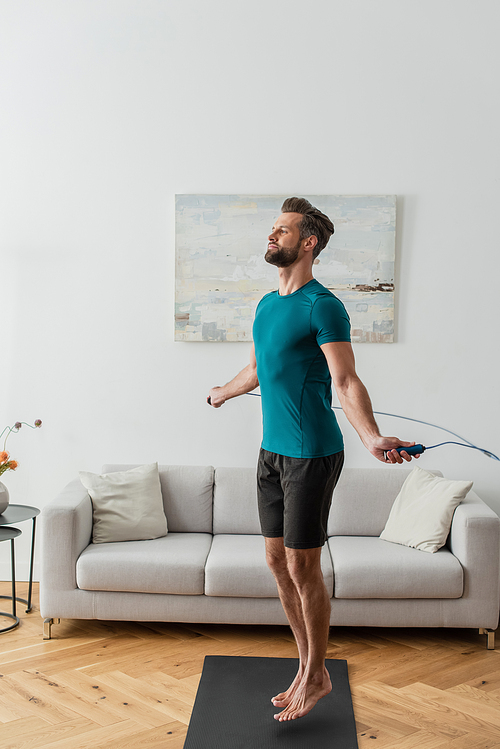 full length view of sportive man jumping with skipping rope at home