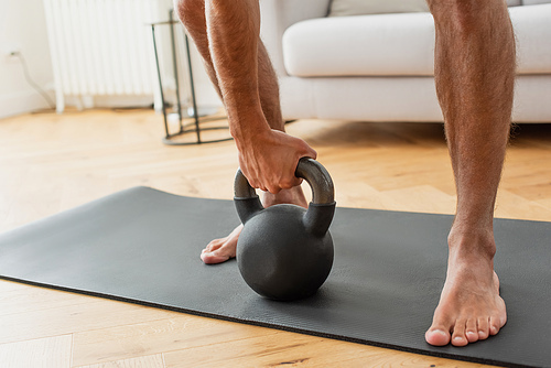 partial view of barefoot sportsman exercising with kettlebell at home