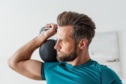 athletic man looking away while exercising with kettlebell at home