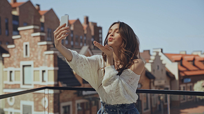 happy young woman taking selfie and sending air kiss