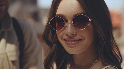 close up of smiling woman in sunglasses near blurred man