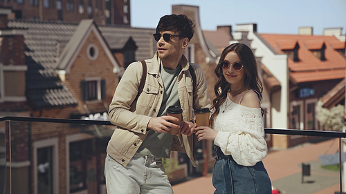 stylish couple in sunglasses holding paper cups outside