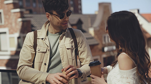 stylish couple in sunglasses holding paper cups and talking outside