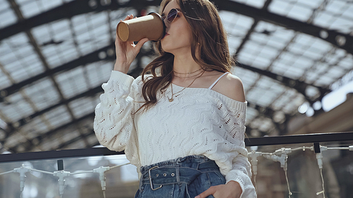 young stylish woman drinking coffee to go in shopping mall
