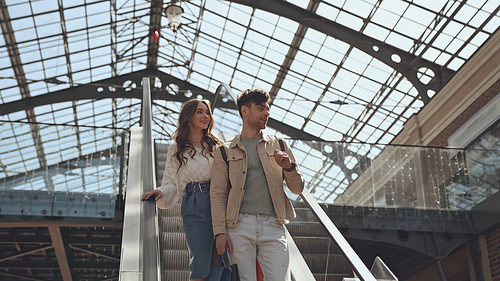 happy man and woman standing on escalator in shopping mall