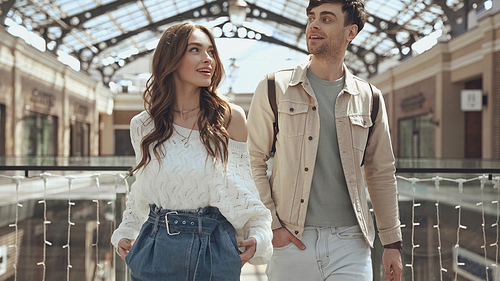 happy woman and man posing with hands in pockets in shopping mall