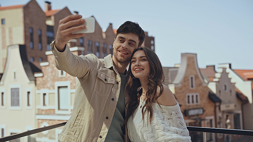 cheerful man taking selfie with happy woman outside