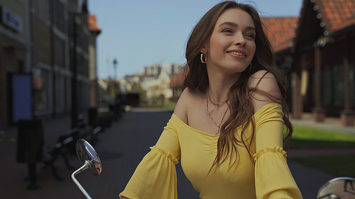 pleased young woman with wavy hair smiling near motorcycle