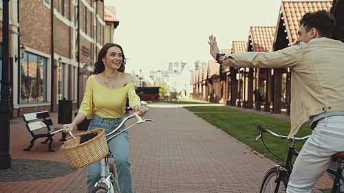 happy man waving hand near woman riding bicycle on street