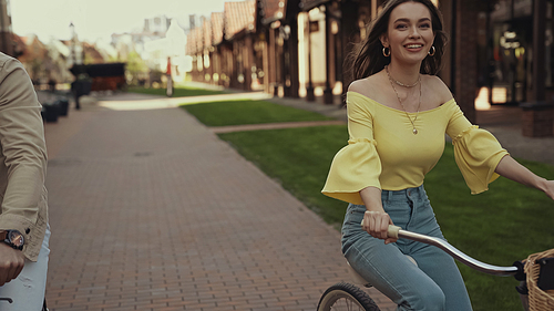 happy woman in blouse riding bicycle near man on street