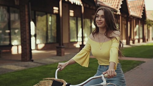 happy young woman in yellow blouse smiling while riding bicycle outside