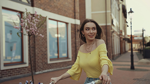 happy young woman in yellow blouse looking away while riding on bicycle outside