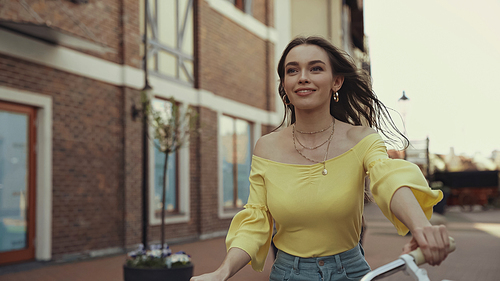 joyful young woman in yellow blouse smiling while riding on bicycle outside