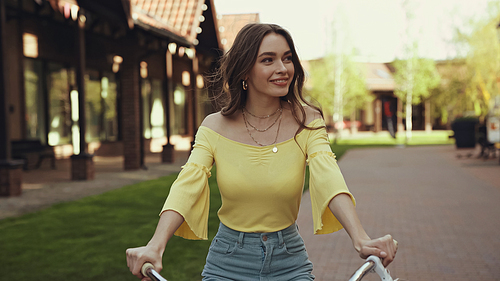 positive young woman in yellow blouse smiling while riding bicycle outside