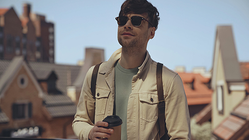 good-looking man in sunglasses holding coffee to go outside