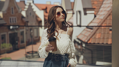stylish young woman in sunglasses holding coffee to go outside