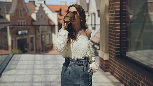 stylish young woman in sunglasses drinking coffee to go outside
