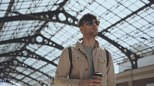 low angle view of stylish man in sunglasses holding coffee to go outside