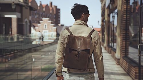 back view of stylish man with leather backpack walking outside