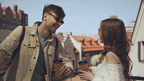 stylish couple smiling while holding paper cups outside