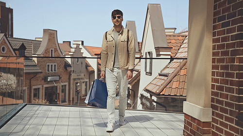 stylish man in sunglasses holding shopping bags and walking outside