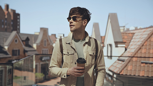 trendy man in sunglasses holding disposable cup with coffee to go outside