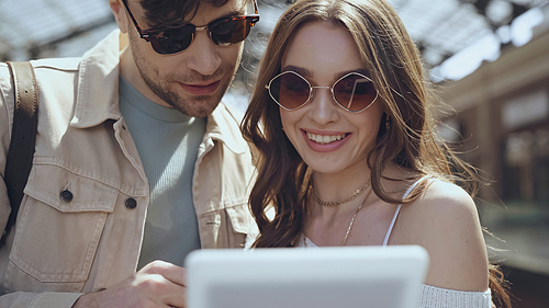 happy man and woman in sunglasses using blurred digital tablet