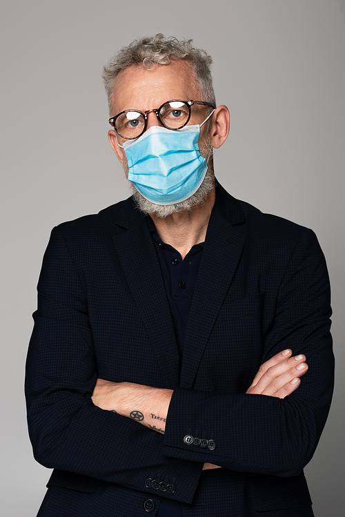 mature man with grey hair in glasses and medical mask posing isolated on grey