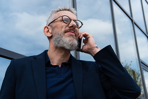 middle aged businessman in glasses with grey hair talking on smartphone near building