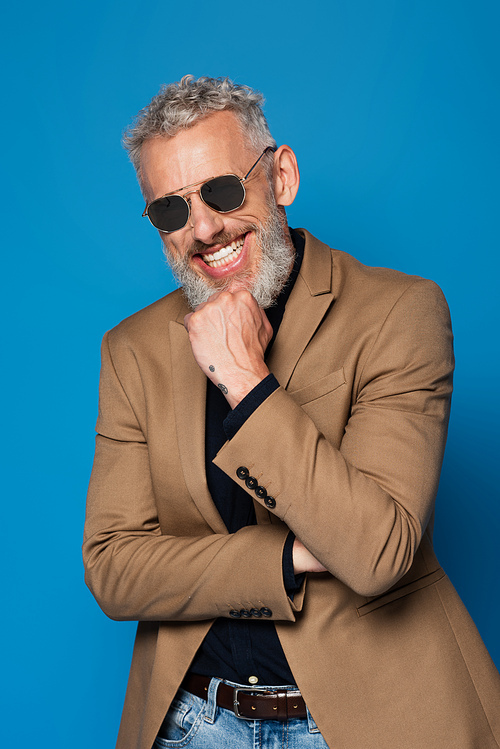 cheerful middle aged man in sunglasses isolated on blue