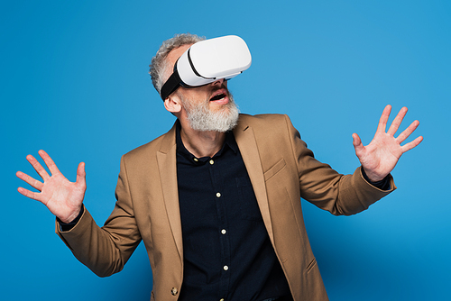 surprised middle aged man in vr headset gesturing on blue