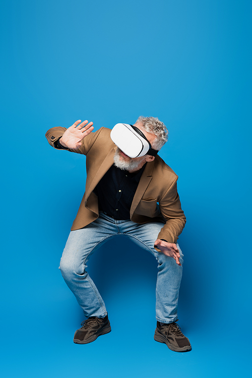 full length of middle aged man in vr headset squatting on blue
